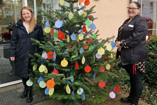 Das Bild zeigt Myriam Haag vom Sozialdienst und Einrichtungsleiterin Natalie Hoss vor dem Wunschbaum