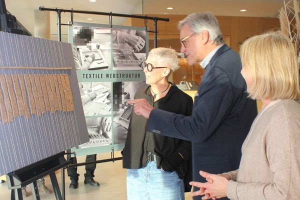 Gesprächsszene Zwei Frauen und ein Mann stehen vor einem Ausstellungsstück. Der Mann zeigt mit dem Finger auf das Stück und die drei Personen unterhalten sich.