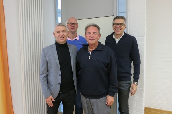 Das Bild zeigt vier Männer die im Anzug vor der Kamera stehen und lächeln