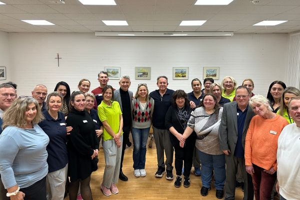 Das Bild zeigt eine sehr große Gruppe von Personen die alle gemeinsam in einem Raum stehen und in die Kamera lächeln