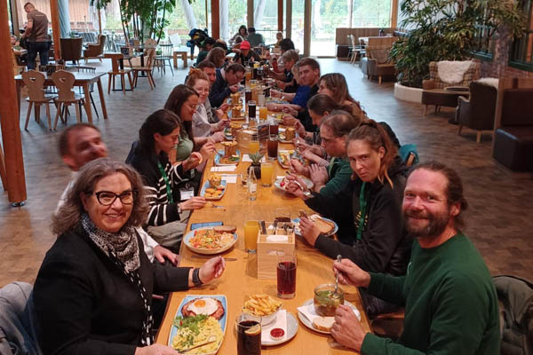 Gemeinsames Mittagessen Eine große Gruppe sitzt an einem Tisch, einzelnen Personen schauen in die Kamera.