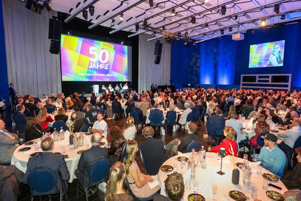 Feier Viele Personen sitzen and runden Tischen und schauen zur Bühne.