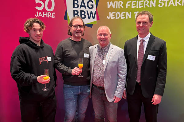 Berlin Vier Personen stehen vor einer bunten Wand und schauen in die Kamera.