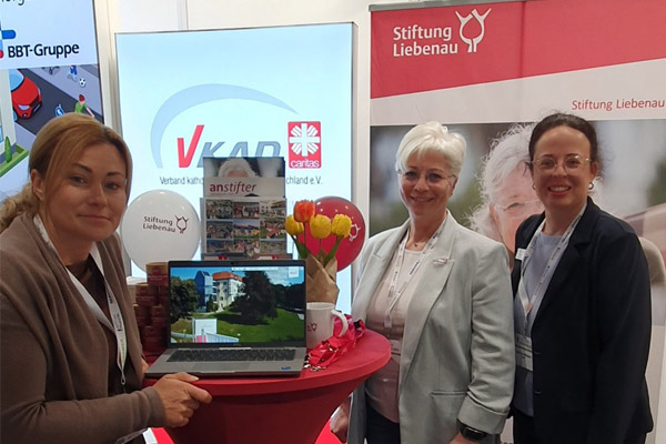 Drei Frauen stehen an einem Messestand und lächeln in die Kamera.