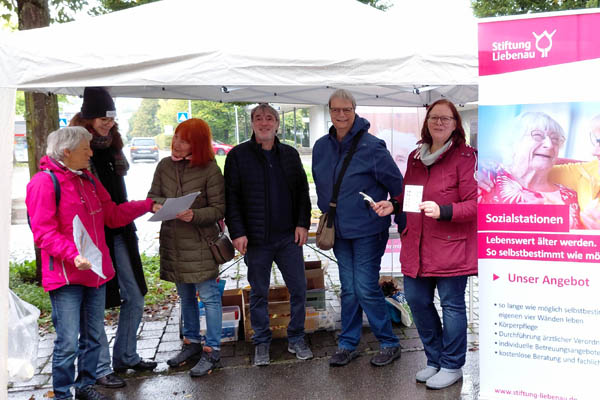 Personen am Marktstand und ein Roll-up der Stiftung Liebenau.
