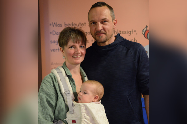 Ein Mann und eine Frau mit Baby in der Trage schauen in die Kamera.