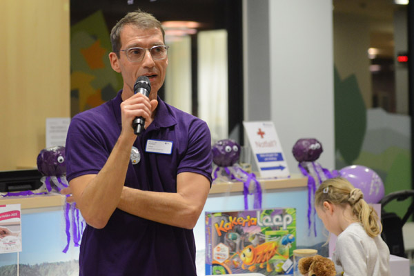 Ein Mann mit Mikrophon spricht, im Hintergrund ist ein spielendes Kind.