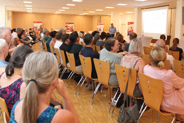 Vielen Zuhörerinnen und Zuhören in einem großen Raum.