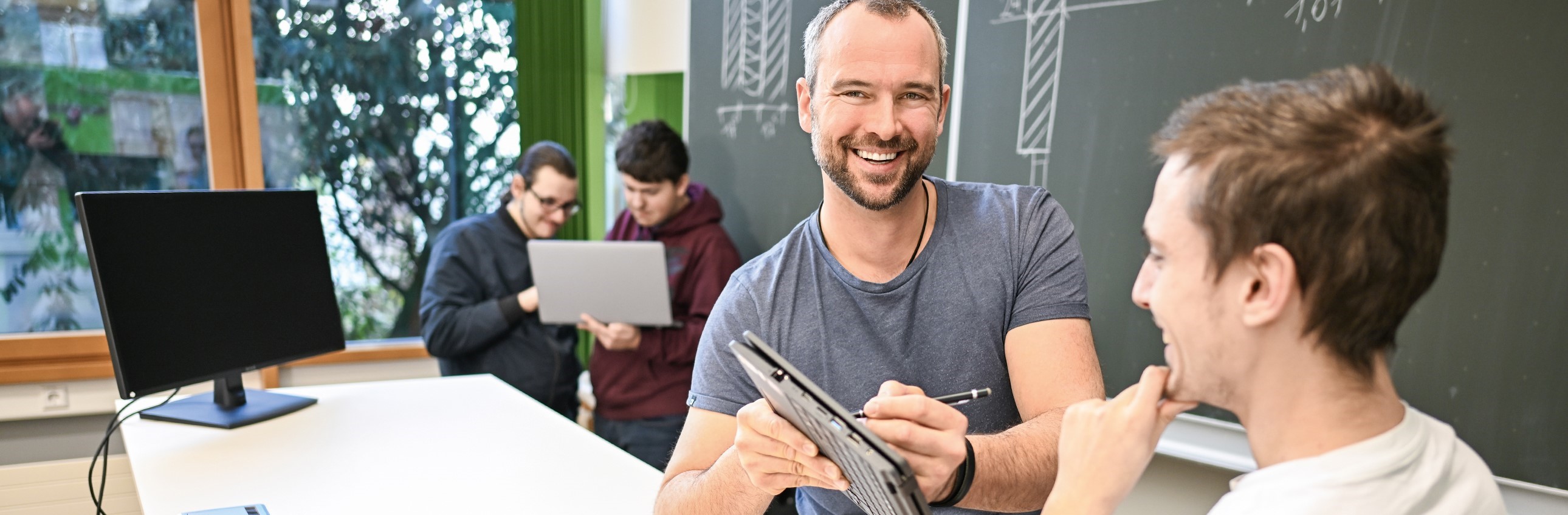 Das Bild zeigt einen Lehrer mit Schüler im Klassenzimmer