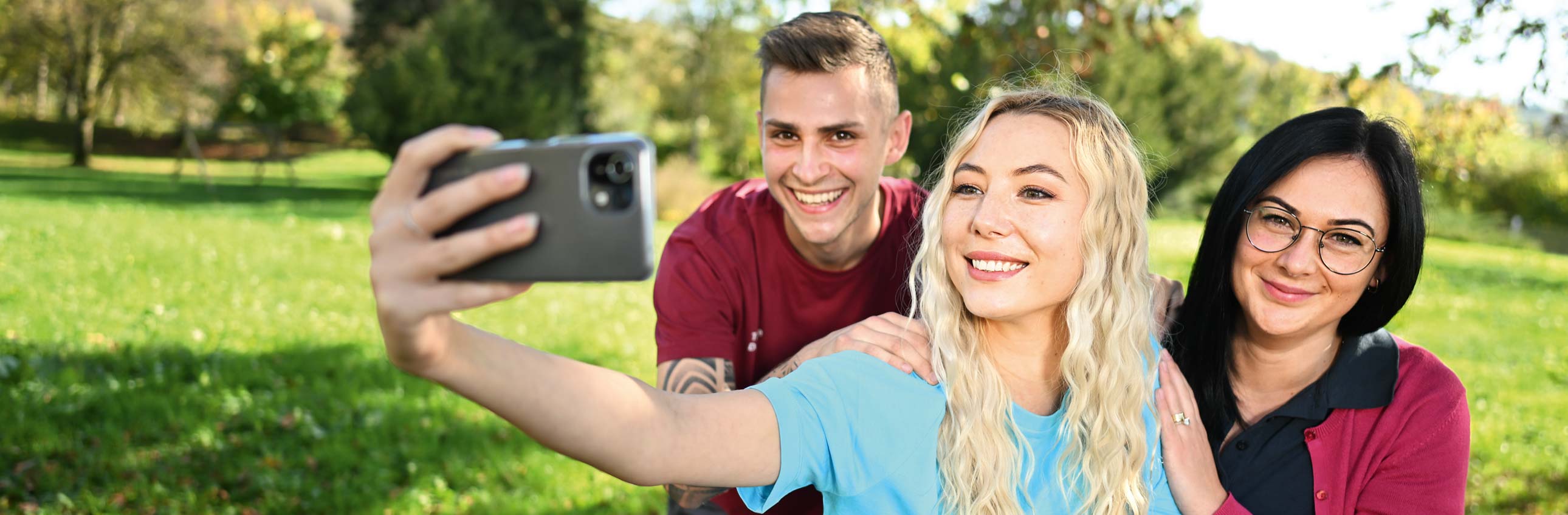 Das Bild zeigt drei junge Menschen bei der Aufnahme eines Selfies