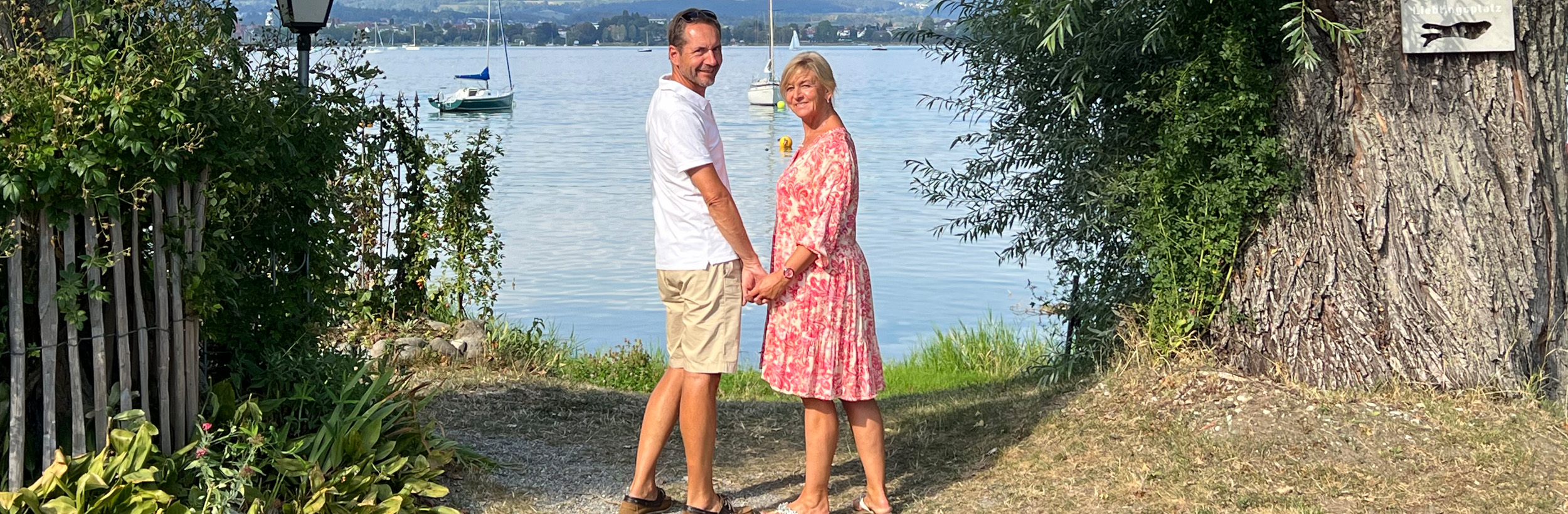 Das Bild zeigt einen Mann und eine Frau händchenhaltend am Seeufer